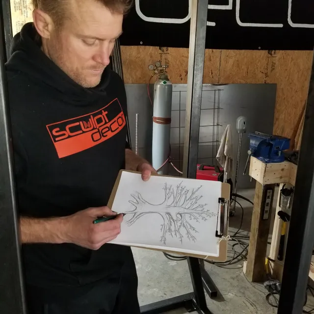 Dustin Weatherby sketching a steel tree sculpture design on a clipboard in his SculptDecor studio