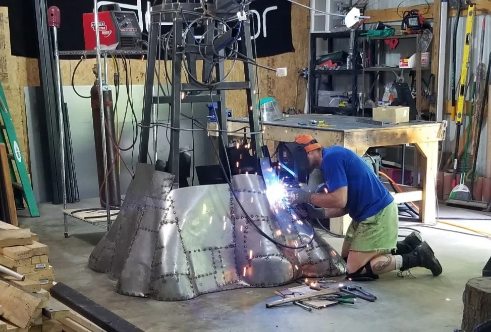 Dustin Weatherby welding the base of a metal tree sculpture in his studio