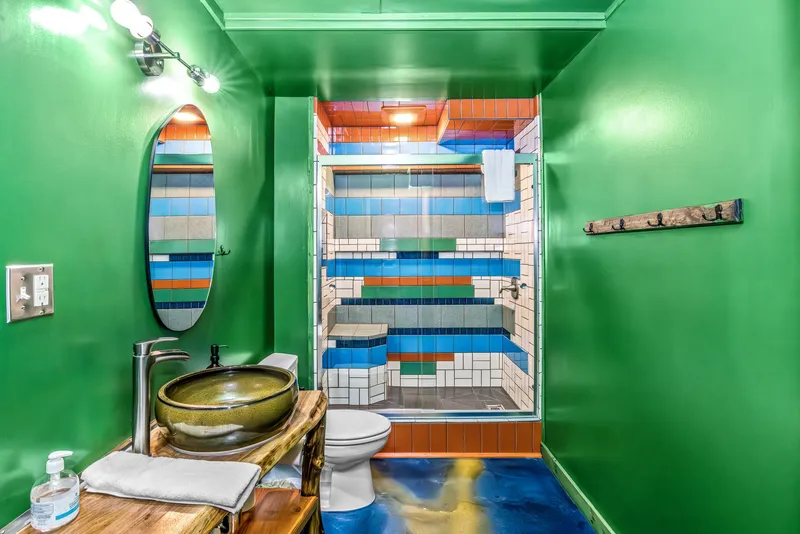 Green bathroom with a striped multicolor tile shower and glazed ceramic vessel sink by Dustin Weatherby