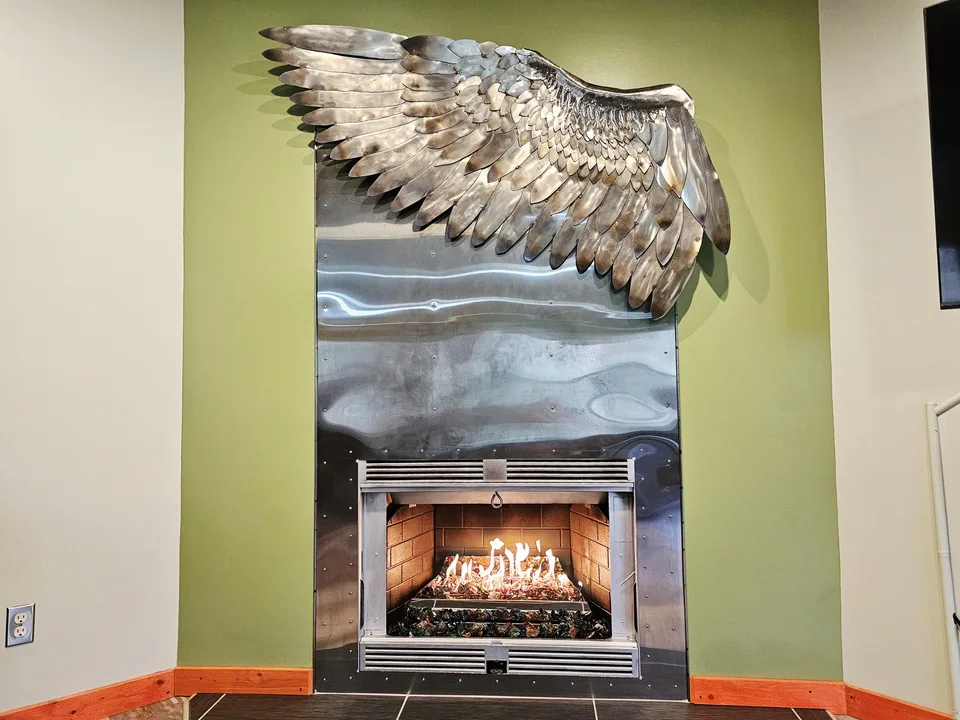 Custom stainless steel hawk-wing fireplace surround installed at Raven's Retreat Art Lodge