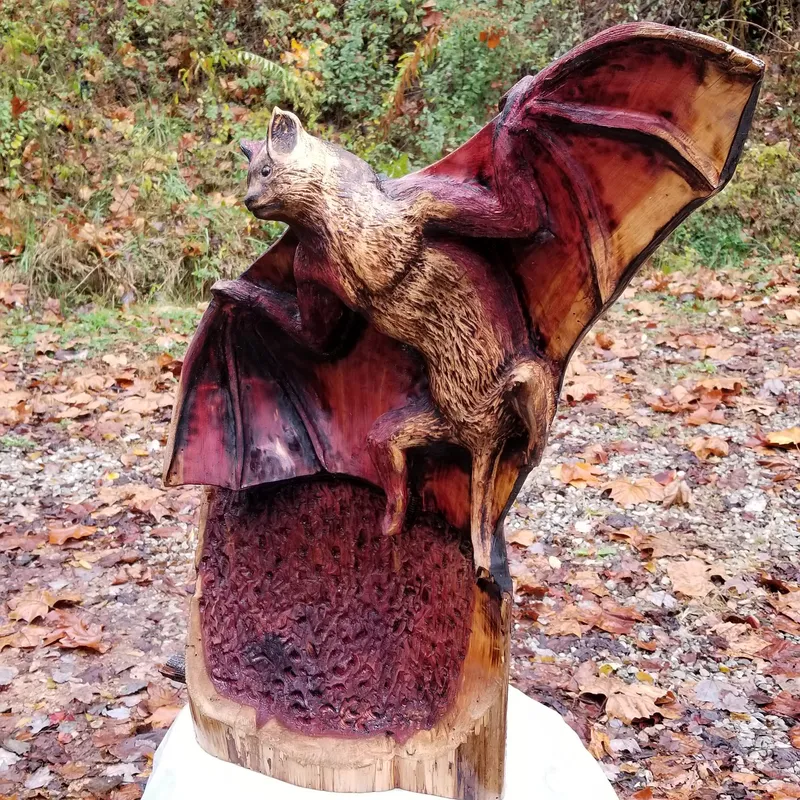 Flame-finished wood bat sculpture with outstretched wings on a stump