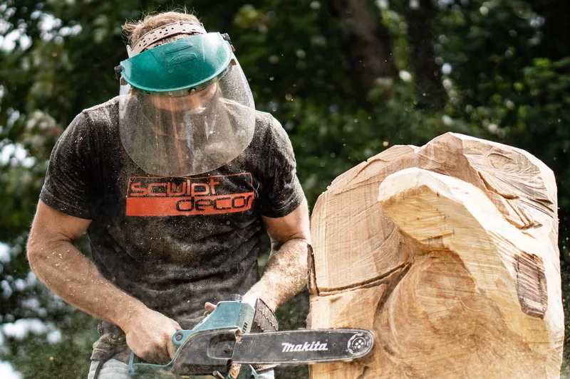 Dustin Weatherby chainsaw-carving a log in a face shield, sawdust flying