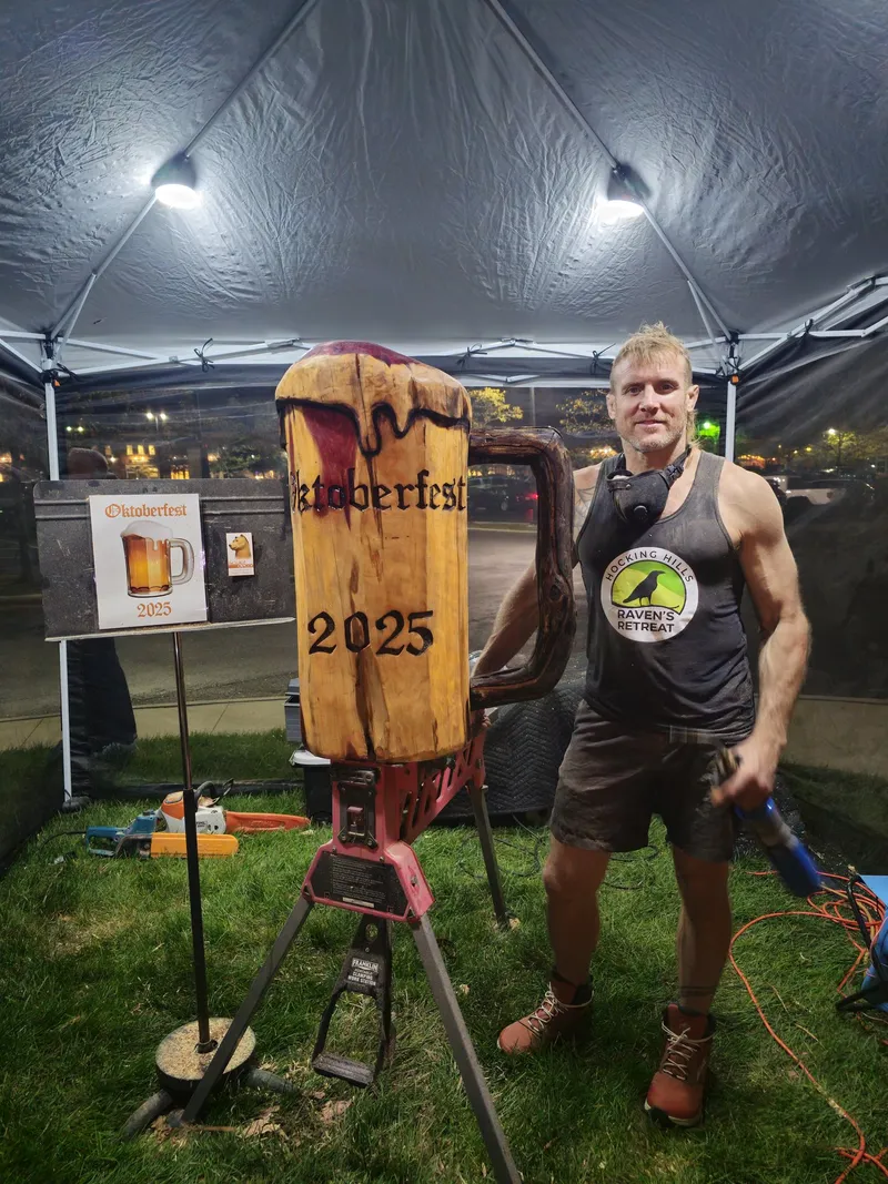 Dustin beside an "Oktoberfest 2025" beer-mug log carving