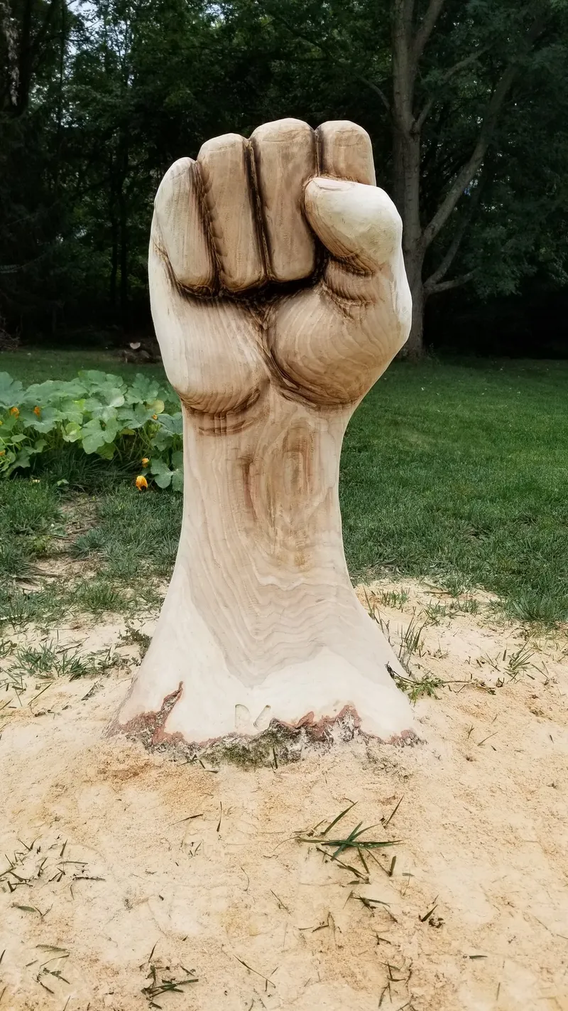 Wood "resist" raised-fist sculpture carved from a tree stump, installed outdoors