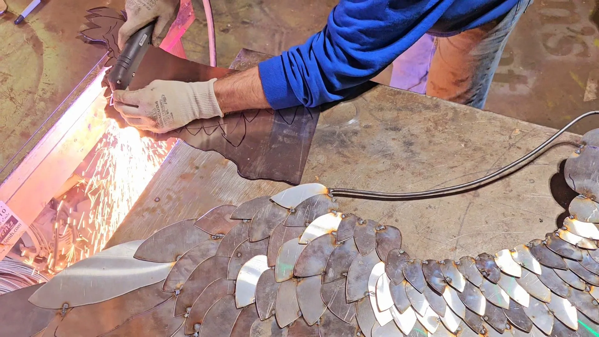 Dustin Weatherby plasma-cutting a scale-feathered metal wing, sparks flying, in his SculptDecor studio