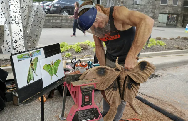 Dustin Weatherby live-carving a wood luna moth sculpture at an outdoor event