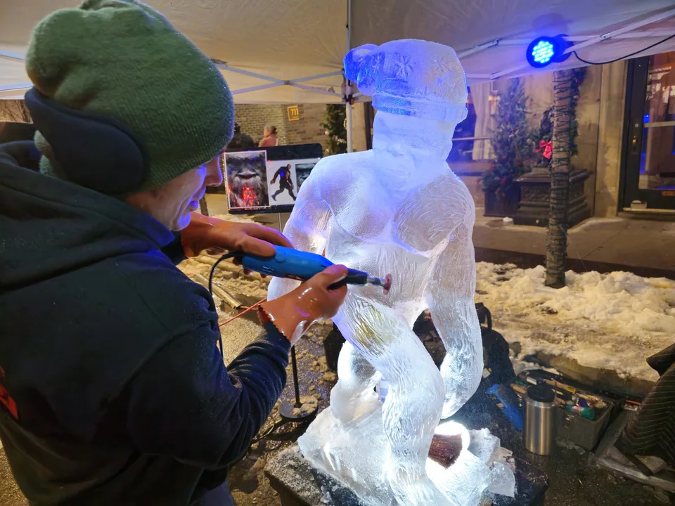 Dustin Weatherby carving a figure from a block of ice under blue event lighting during a wedding celebration